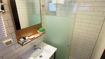 A bathroom with a white sink, a mirror, a glass shower enclosure, and a small shelf with toiletries.