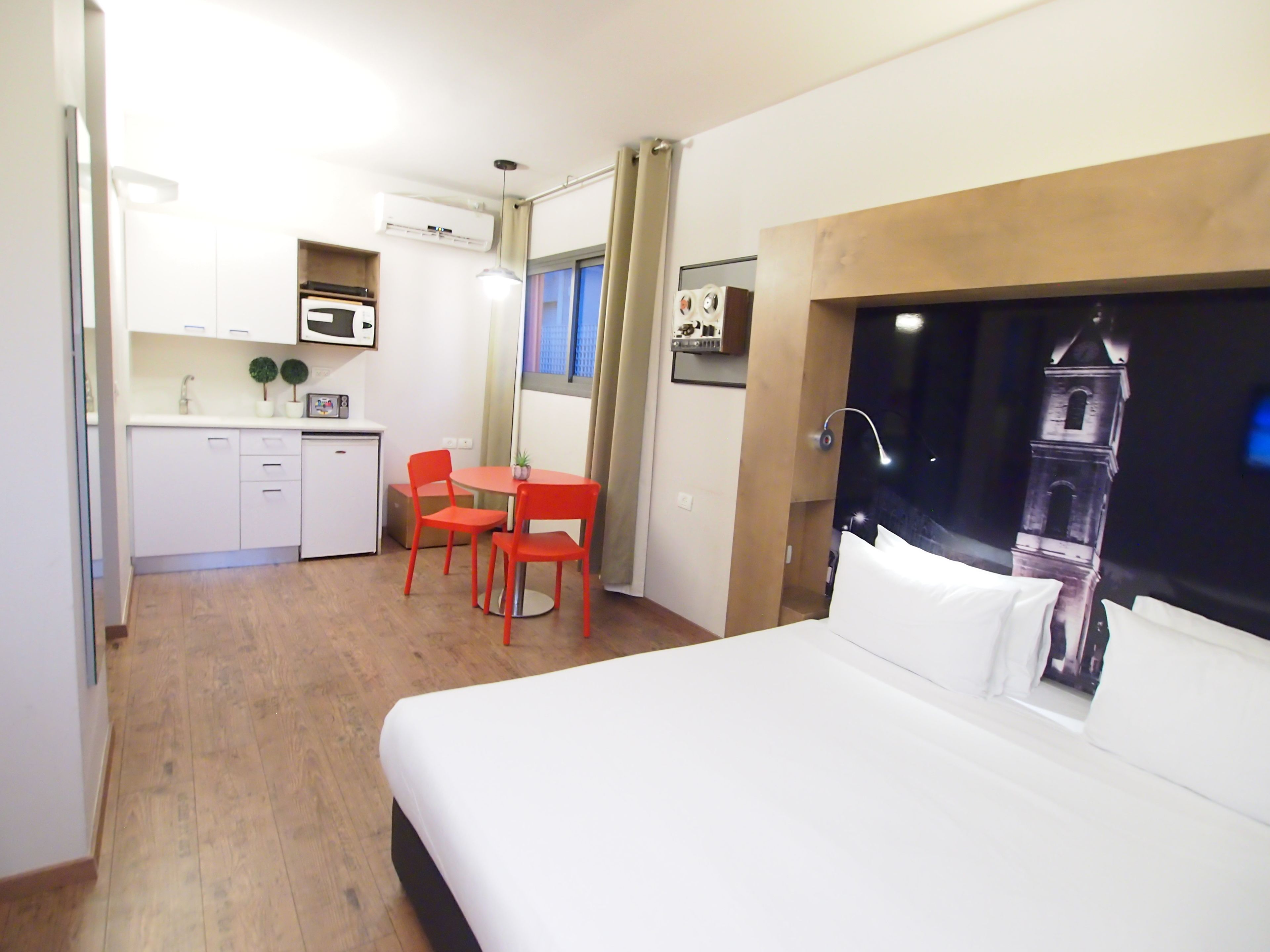 Habitación de hotel con una cama, un escritorio con dos sillas, una kitchenette y vistas a una torre.