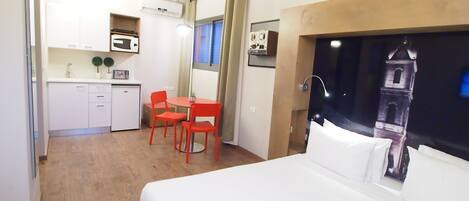 Habitación de hotel con una cama, un escritorio con dos sillas, una kitchenette y vistas a una torre.