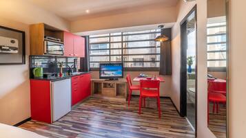 A compact kitchen with red cabinets, a wooden countertop, and a television.
