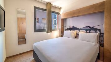 A hotel room with a large bed, a mirror, a window with curtains, and a wooden headboard.
