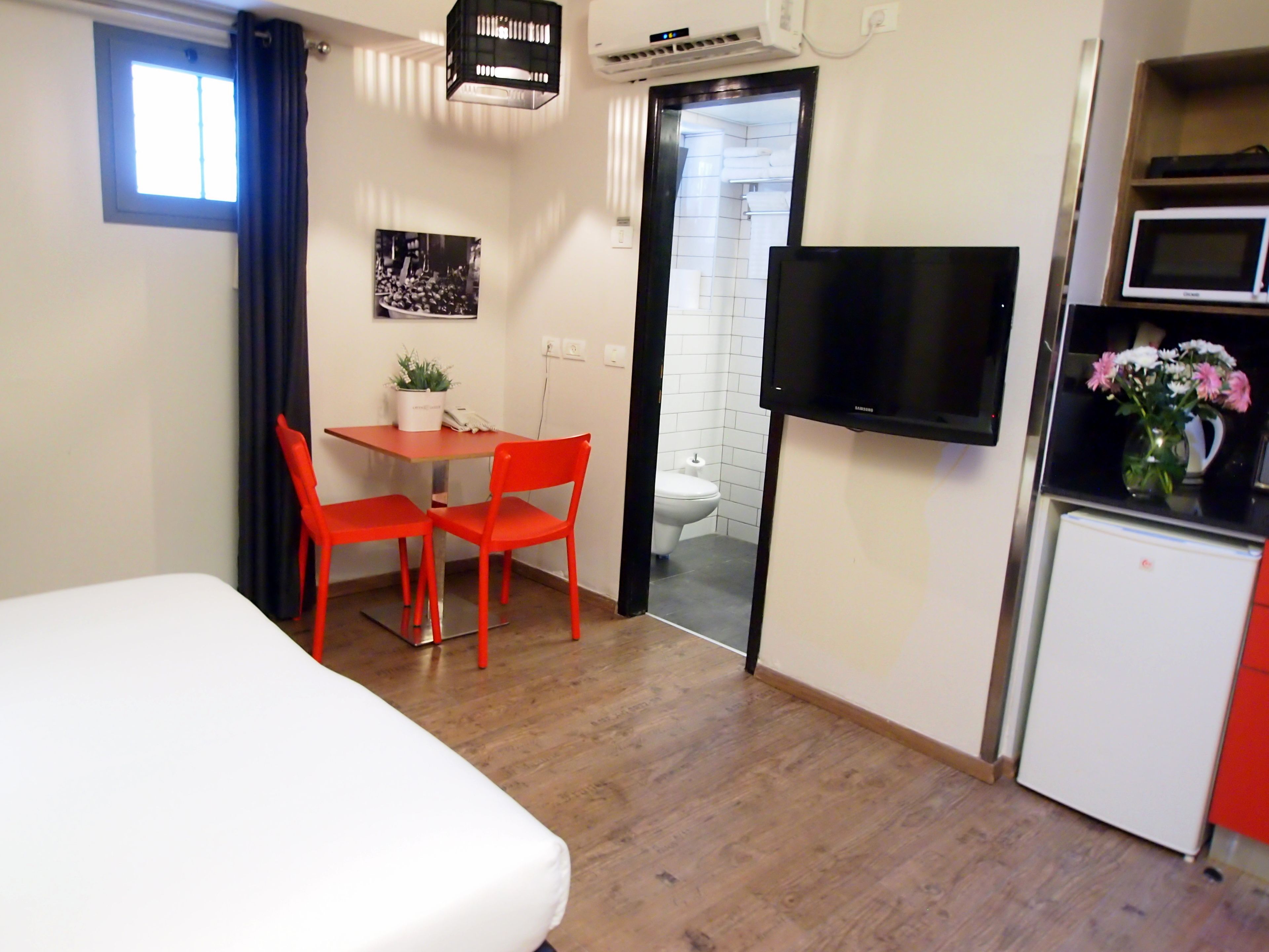 Habitación de hotel con cama, una mesa de comedor con dos sillas, televisión, microondas y refrigerador.