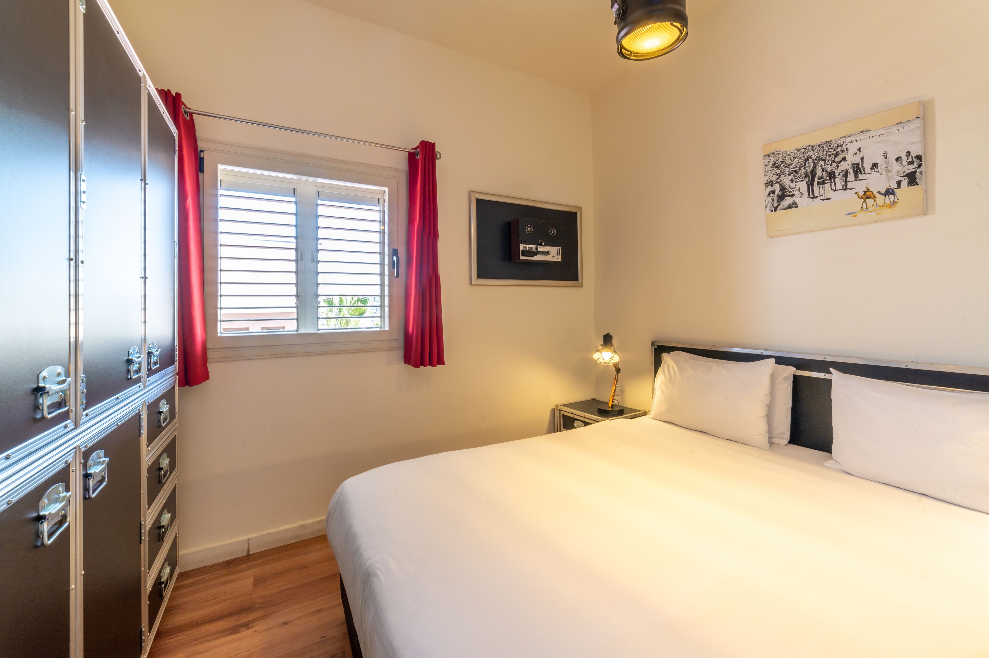 Un dormitorio con cama, mesita de noche, lámpara, armario y ventana con cortinas.