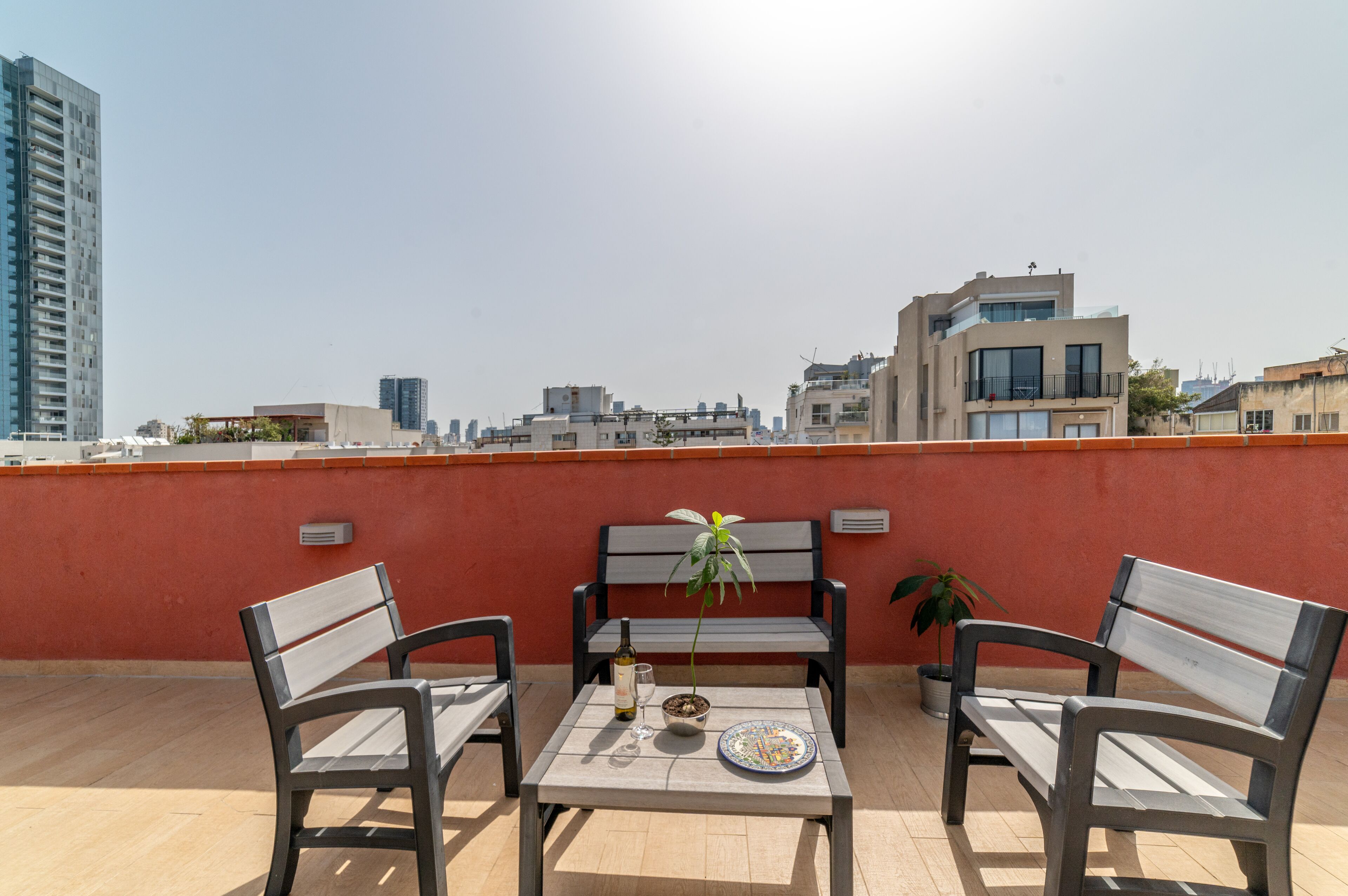 Eine Dachterrasse mit zwei Holzbanken, einem Tisch, einem Blumentopf, einer Weinflasche und einem Glas.