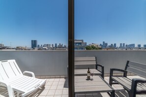 A rooftop terrace with a city skyline view, featuring a table with a bottle and glass, and two benches. - Ben Yehuda Apartments (Tel Aviv)