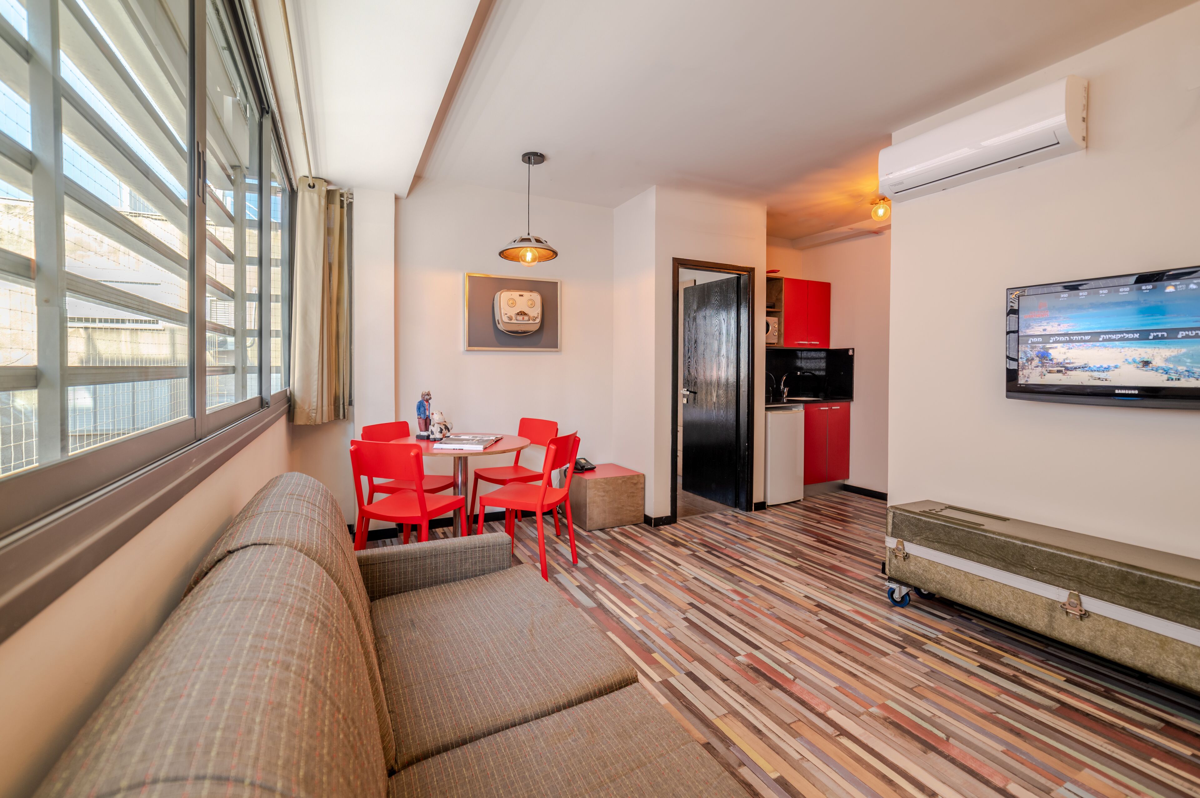 A compact hotel room with a sofa, dining table with chairs, a television, and a patterned floor.