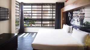 A hotel room with a large bed, a TV mounted on the wall, and a window with blinds. - Ben Yehuda Apartments (Tel Aviv)