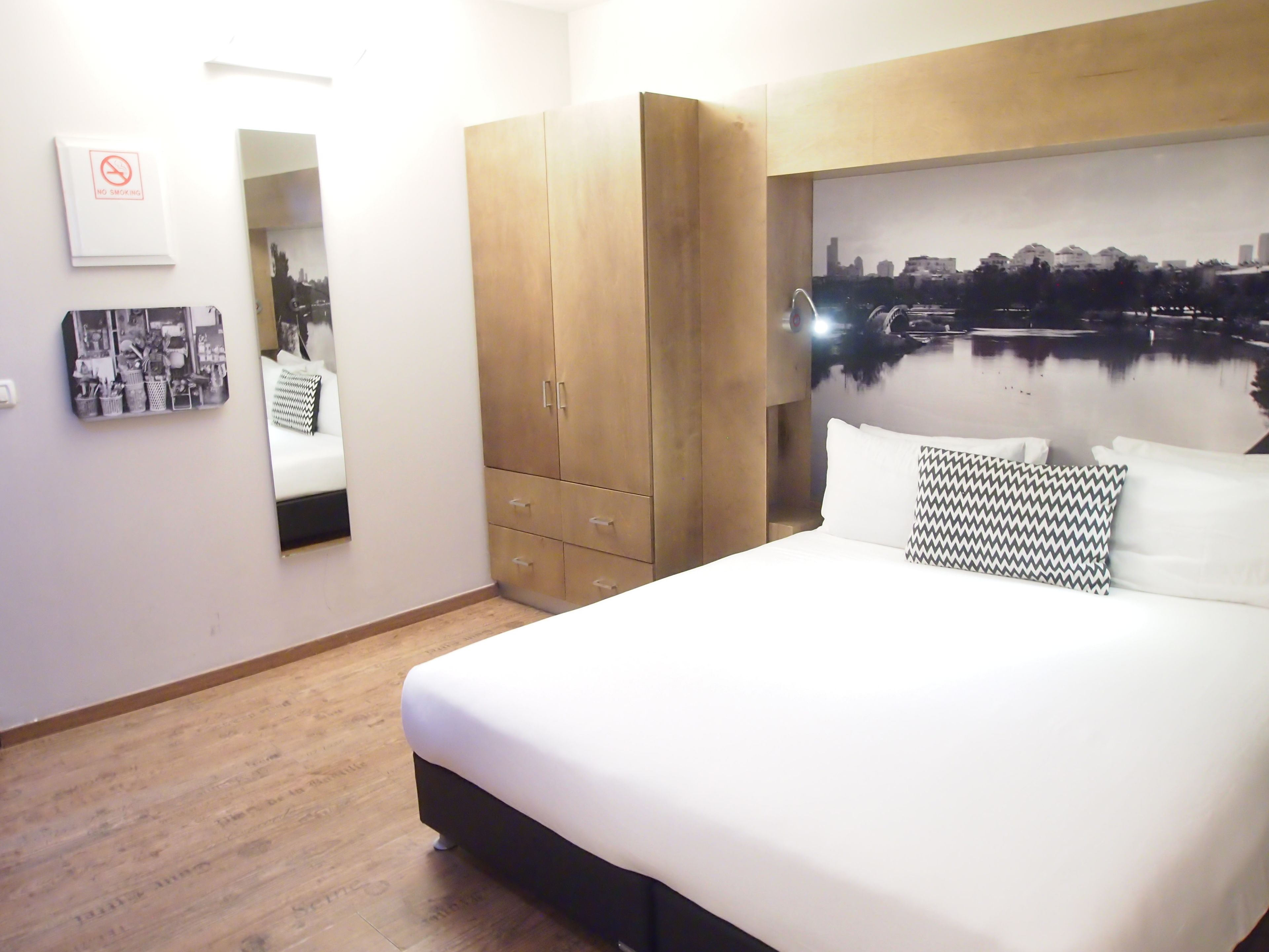 A hotel room with a bed, a wardrobe, a mirror, and a cityscape view.