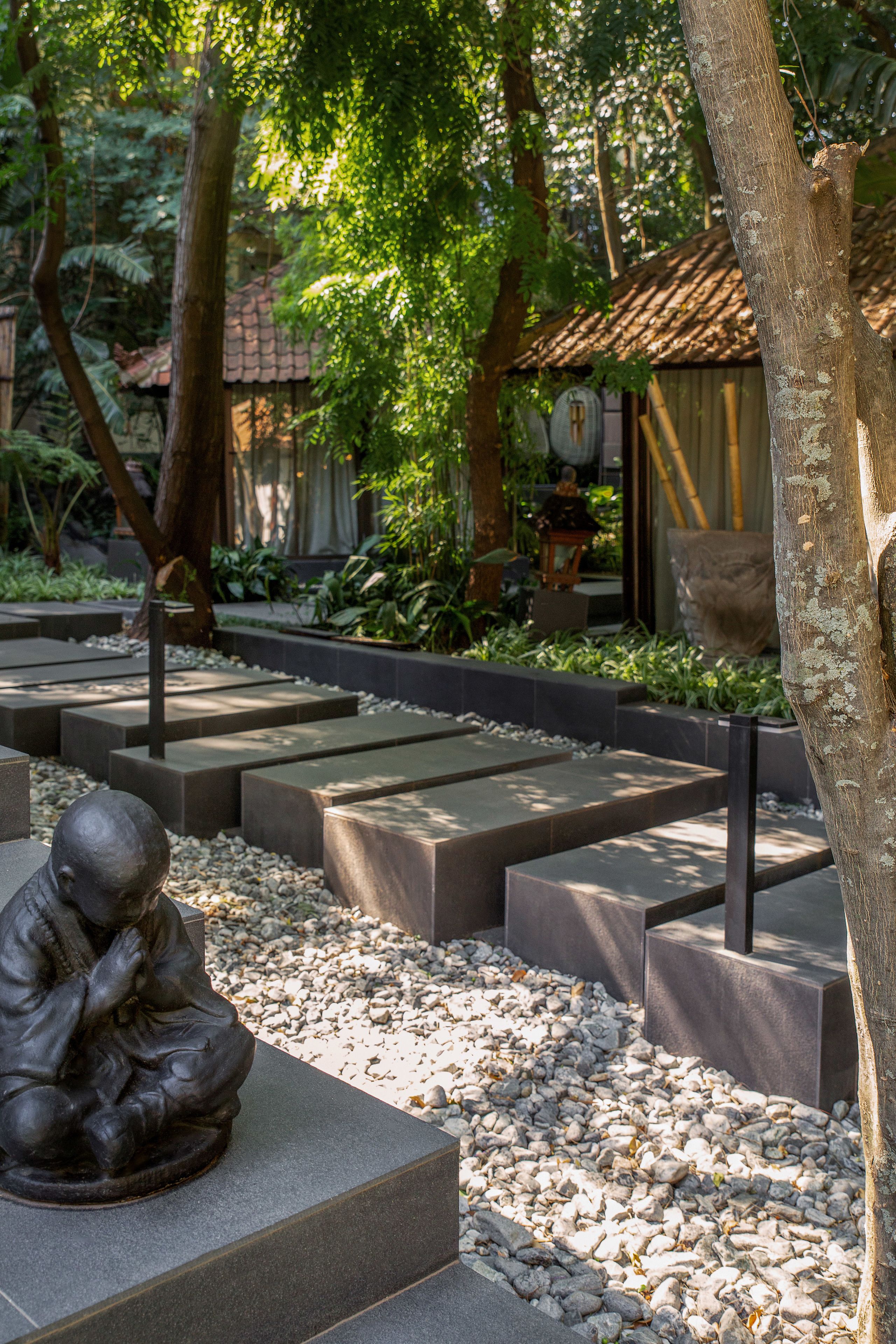 Un jardín sereno con un camino de piedra, una escultura y un edificio tradicional con tejado de baldosas.