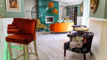 A modern living room with a teal brick wall, a fireplace, and a mix of bar stools and a floral armchair.