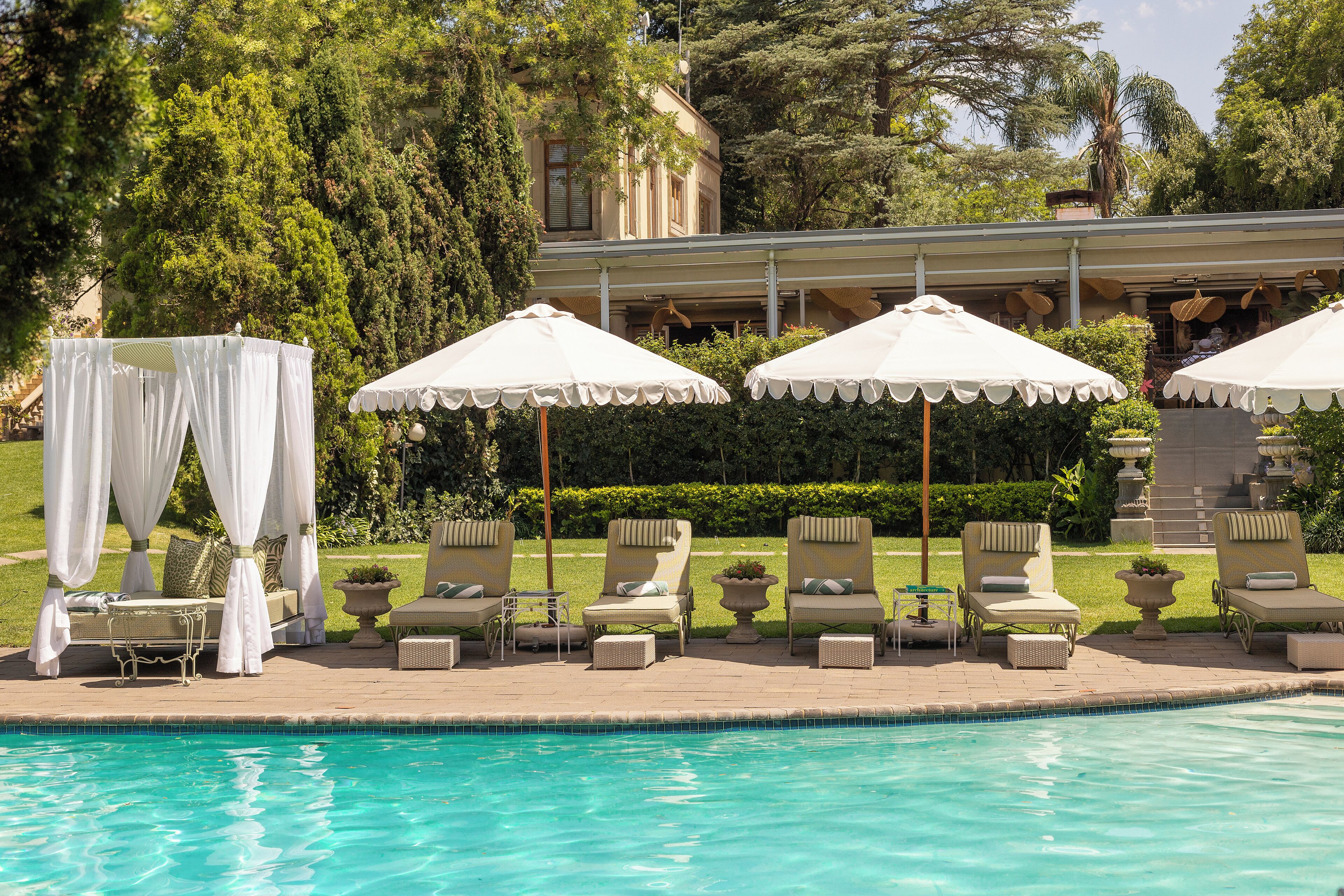 Zona junto a la piscina con sillas de descanso y sombrillas, una cabaña y un edificio al fondo.