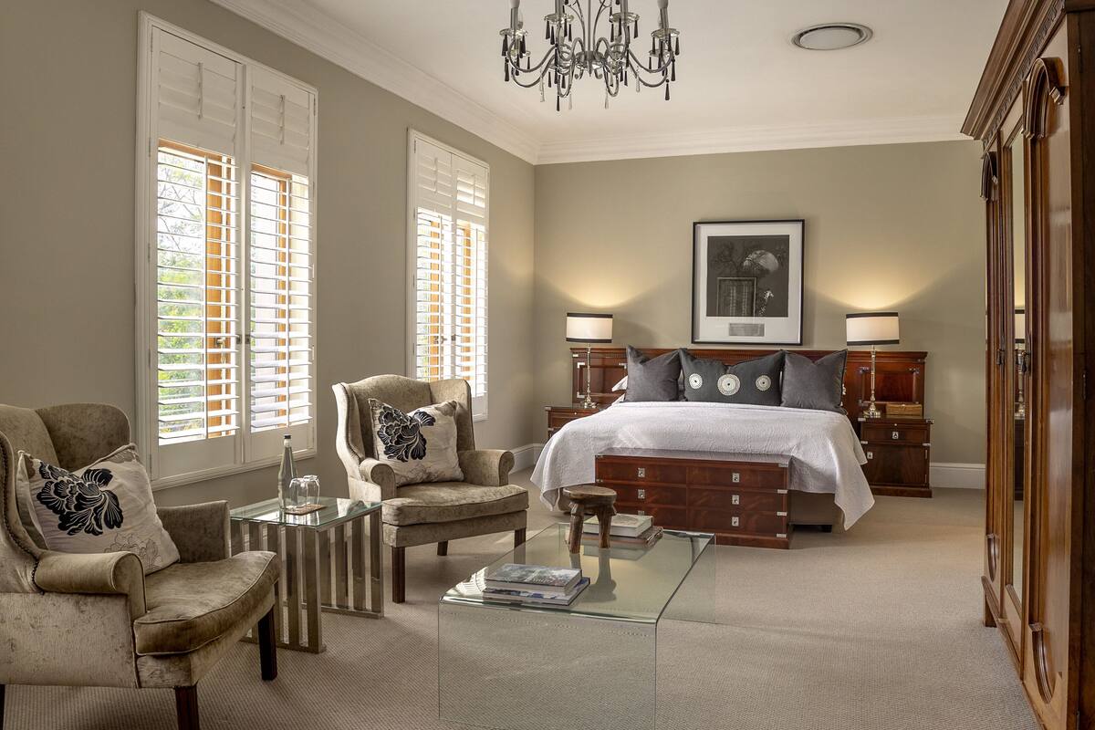 Une chambre spacieuse avec un grand lit, deux tables de chevet avec des lampes, un fauteuil, une table basse en verre et une commode.