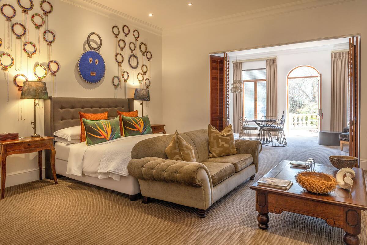 Une chambre élégamment aménagée, dotée d’un grand lit, d’un canapé et d’un coin repas visible à travers une porte ouverte.