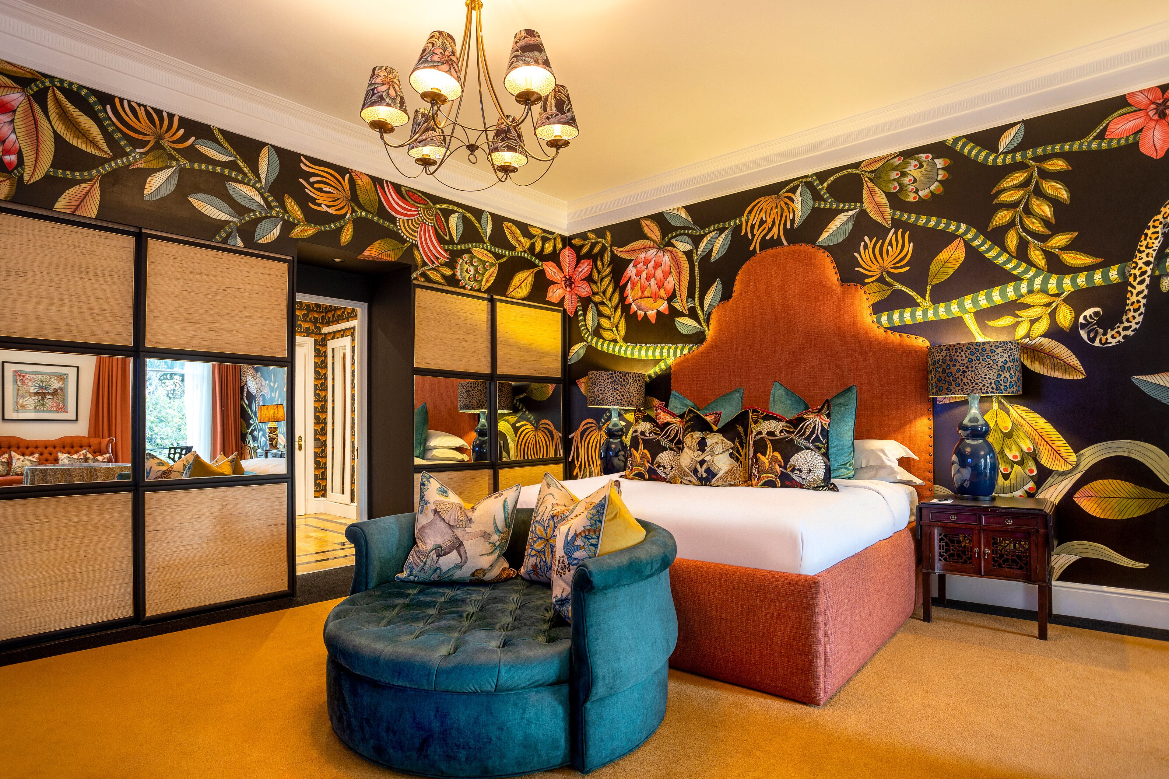 A bedroom with a large bed, a blue armchair, and a vibrant floral wall mural.