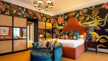 A bedroom with a large bed, a blue armchair, and a vibrant floral wall mural.