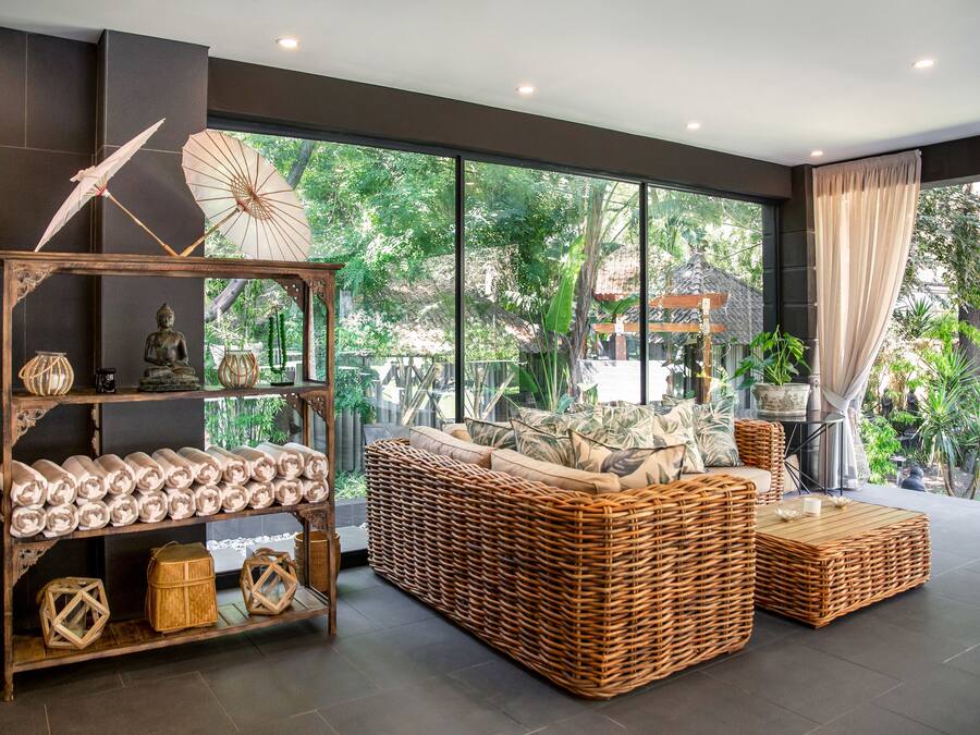 Un salón moderno con un sofá de mimbre, un estante de madera con objetos decorativos y vistas a un exuberante follaje exterior.