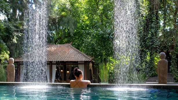 A woman in a pool with water jets, a gazebo, and lush greenery.