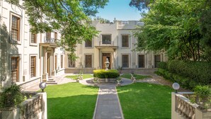 A courtyard with a central fountain, surrounded by a manicured lawn and a building with multiple windows and doors.