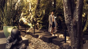 A man walking on a stone pathway in a garden with a statue and various plants.