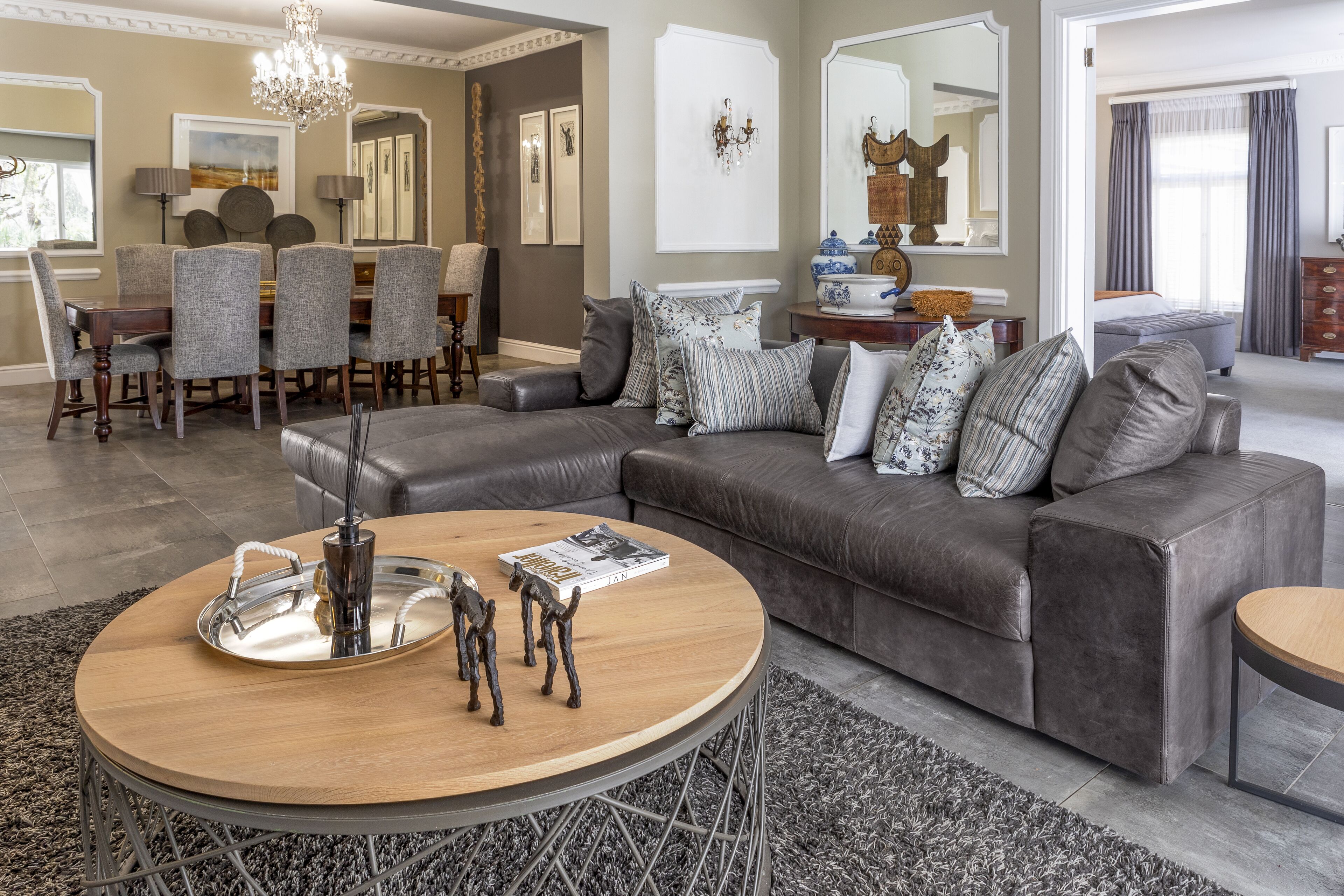 A modern living room with a sectional sofa, a round coffee table, and a dining area with a chandelier.