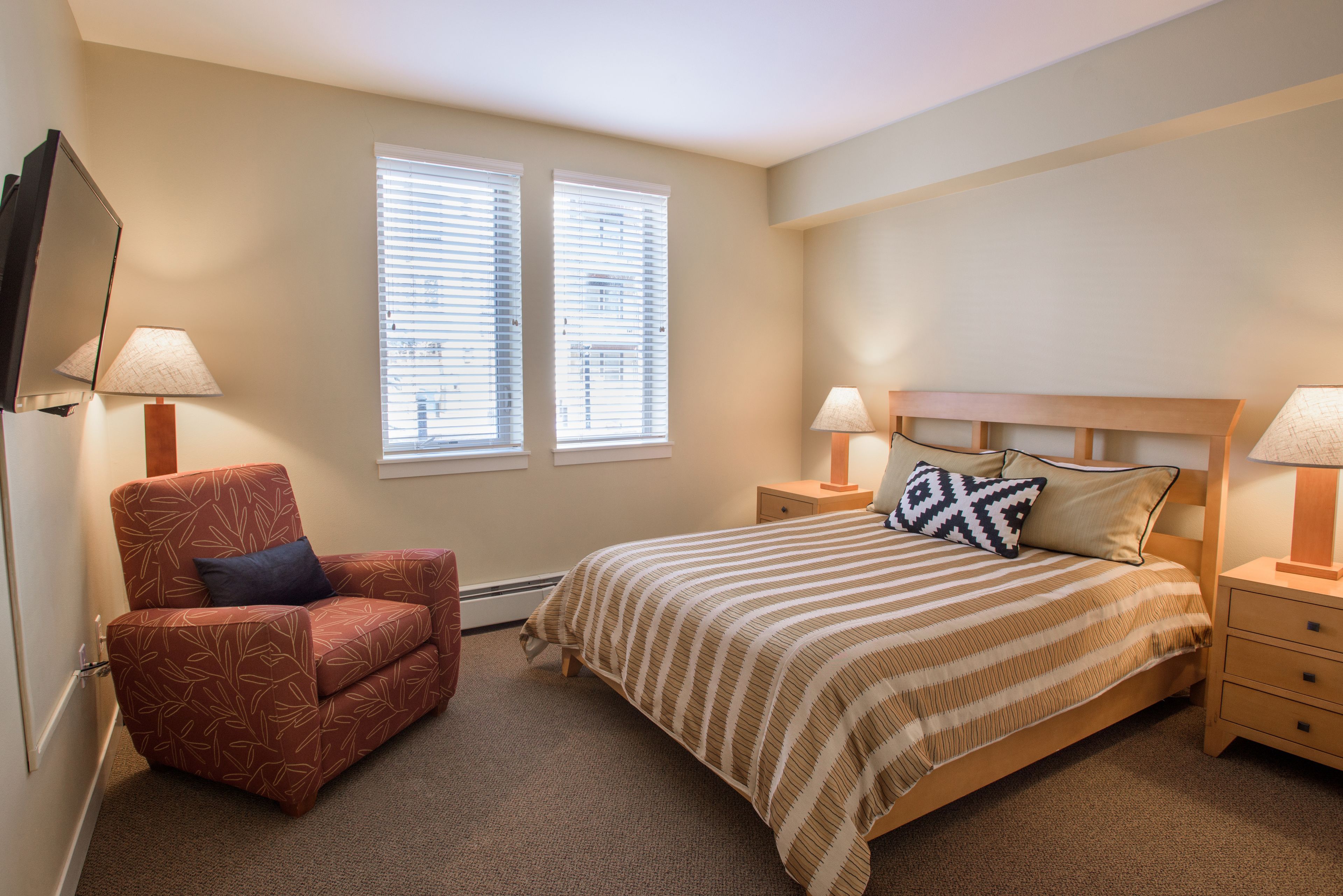 Une chambre à coucher comprenant un lit, une chaise, deux tables de chevet et un téléviseur fixé au mur.