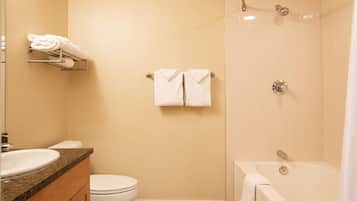 Un baño con inodoro, lavamanos y bañera. Hay toallas colgadas en un perchero y una cortina de ducha.
