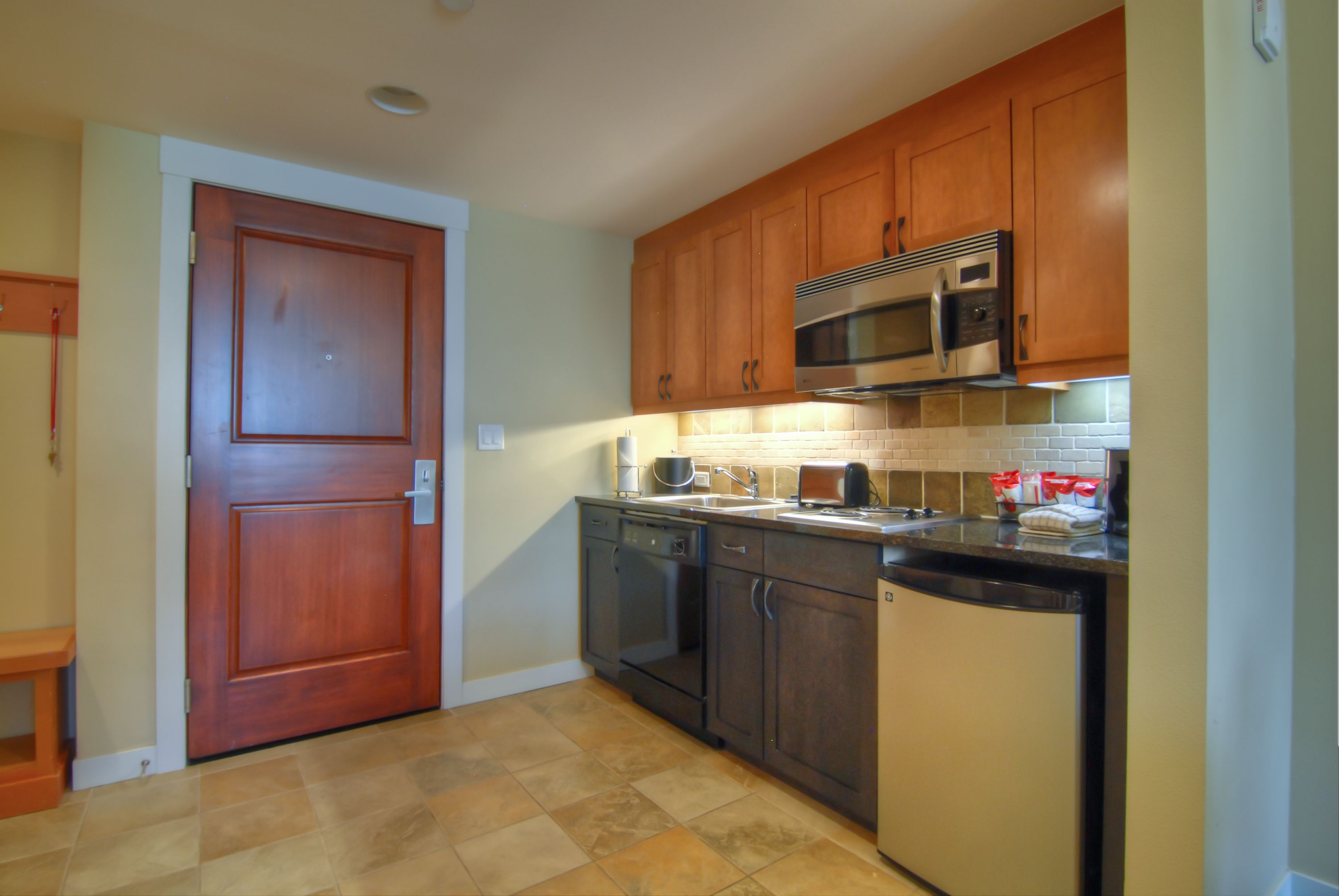 A kitchen with wooden cabinets, a microwave, a dishwasher, and a tiled backsplash.