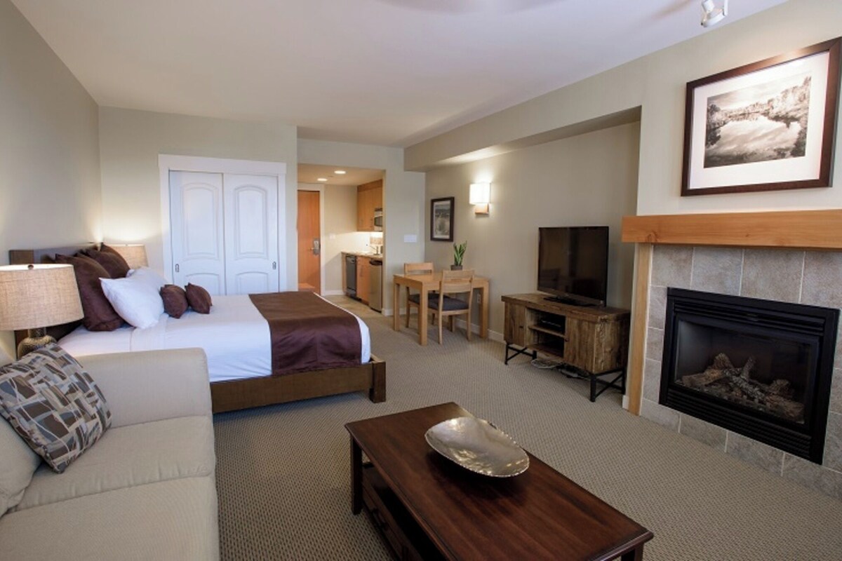 Una habitación de hotel con cama, sofá, televisión, chimenea y zona de comedor.