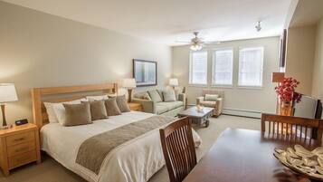 A well-lit bedroom with a large bed, a sofa, a dining table, and a ceiling fan.