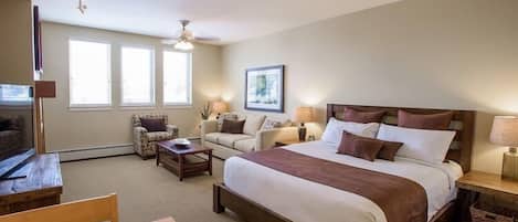 A bedroom with a large bed, two sofas, a wooden table, and a TV.