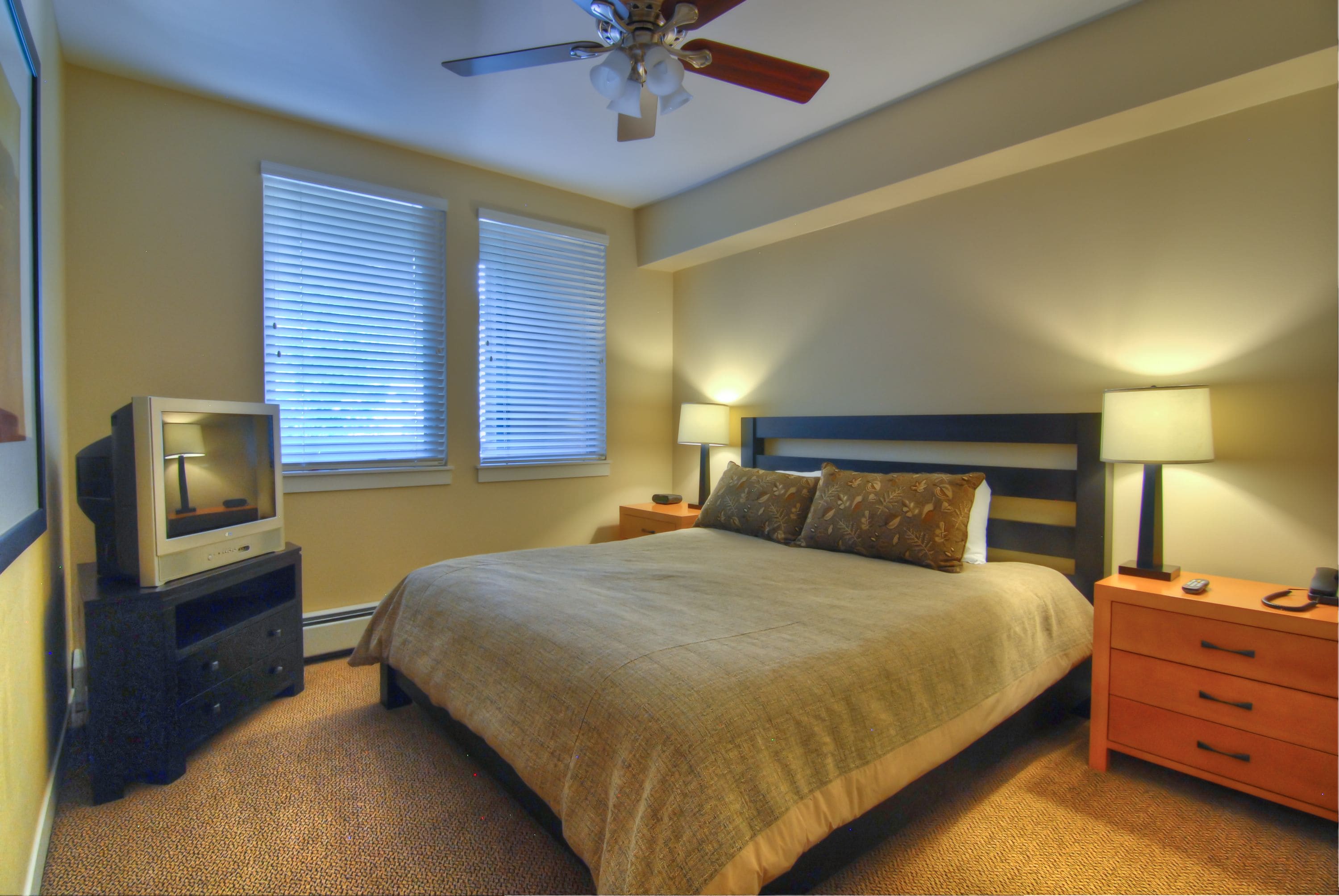 A bedroom with a bed, two bedside tables, a ceiling fan, and a television on a stand.