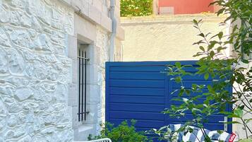 A narrow outdoor patio with a table set for breakfast, surrounded by white metal chairs and a blue gate.
