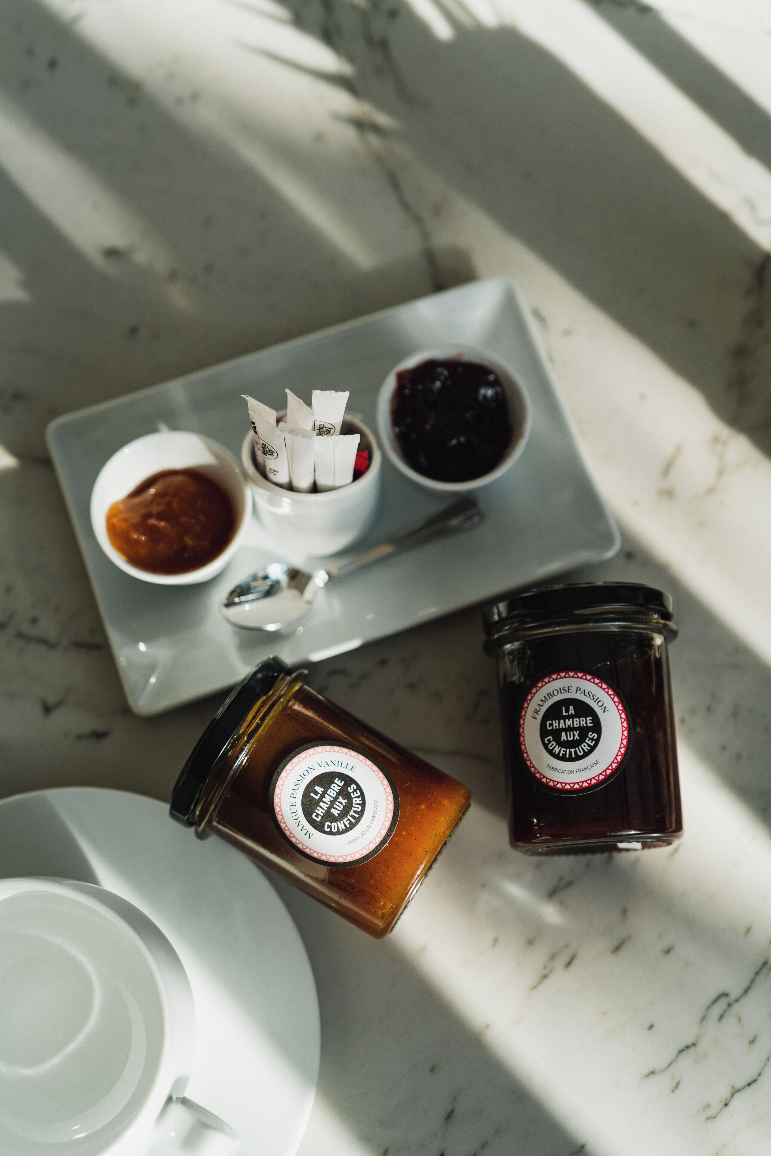 A tray with two jars of jam and a spoon on a marble surface.