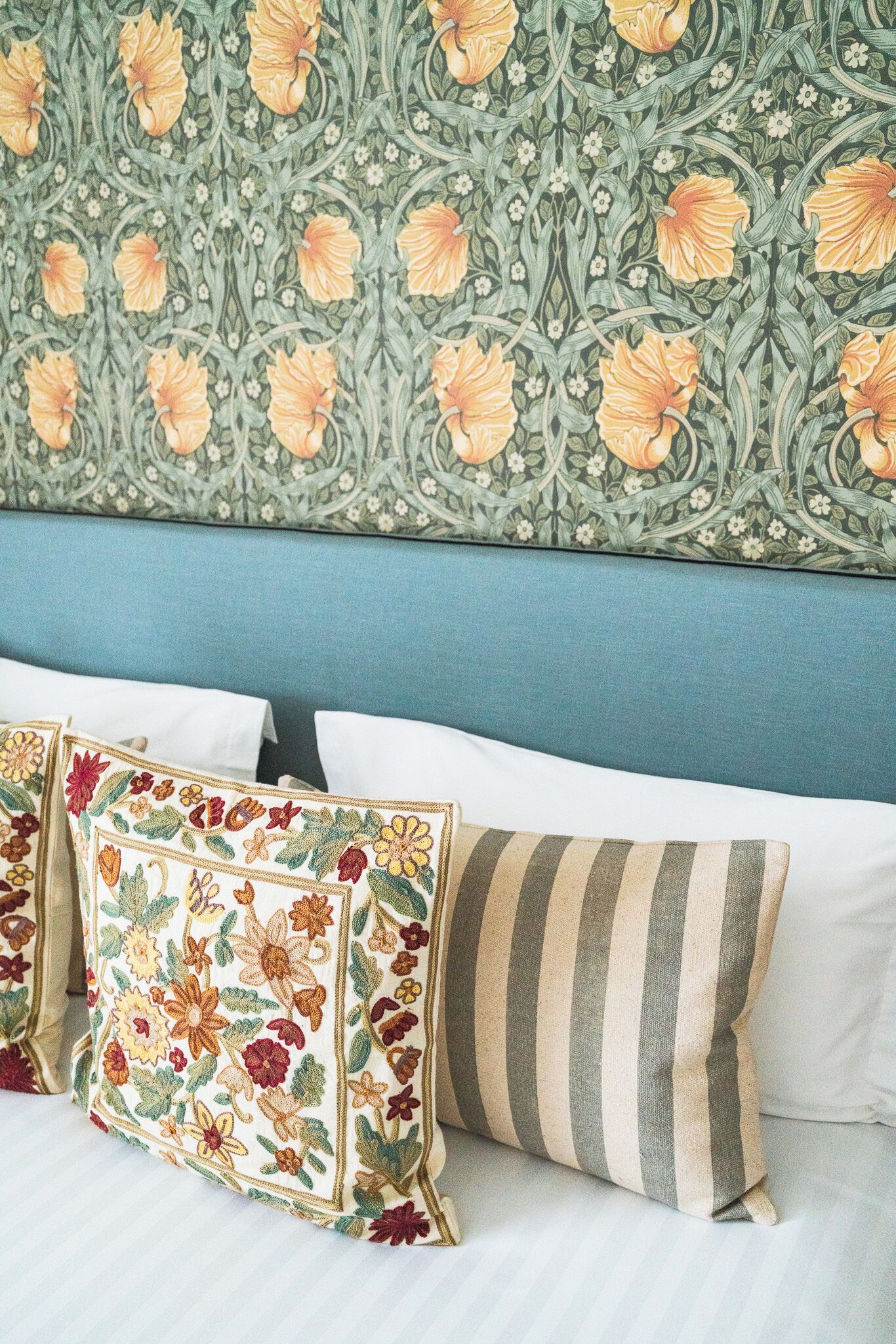 A bed with white linens, a blue headboard, and decorative pillows with floral patterns.