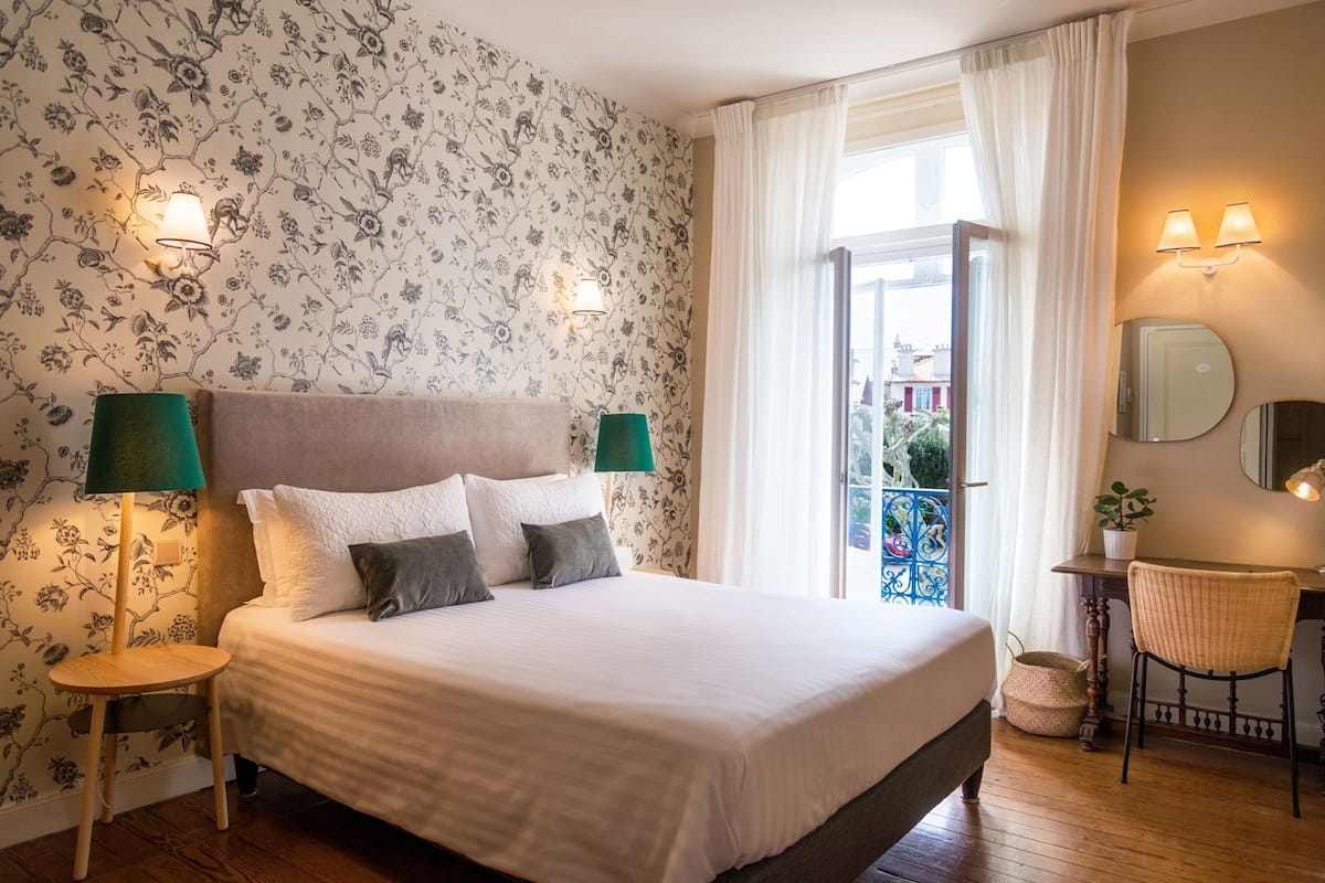 A bedroom with a bed, two bedside lamps, a chair, a small table, and a balcony door.