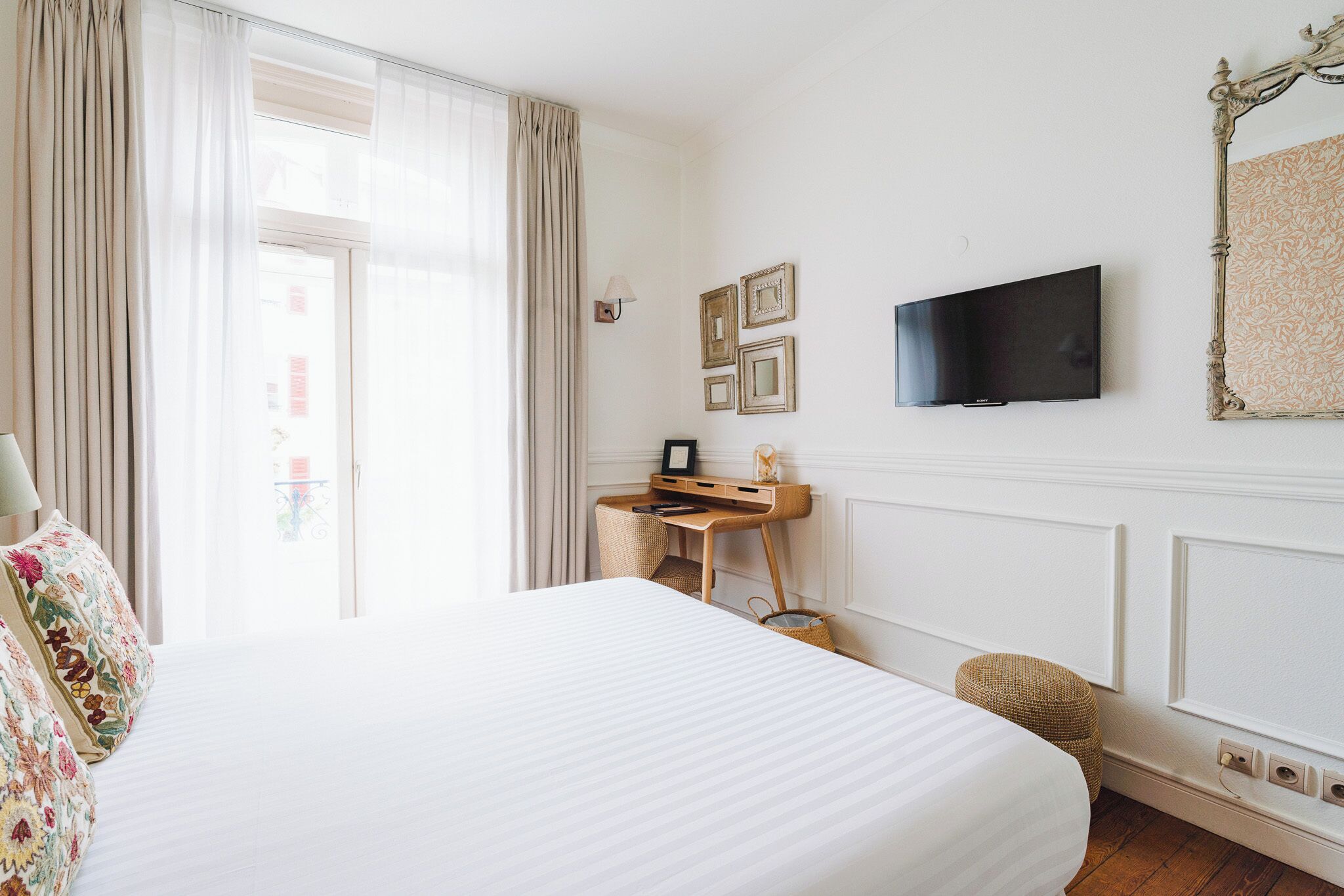 A hotel room with a large bed, a desk with a computer, a television, and a window with curtains.
