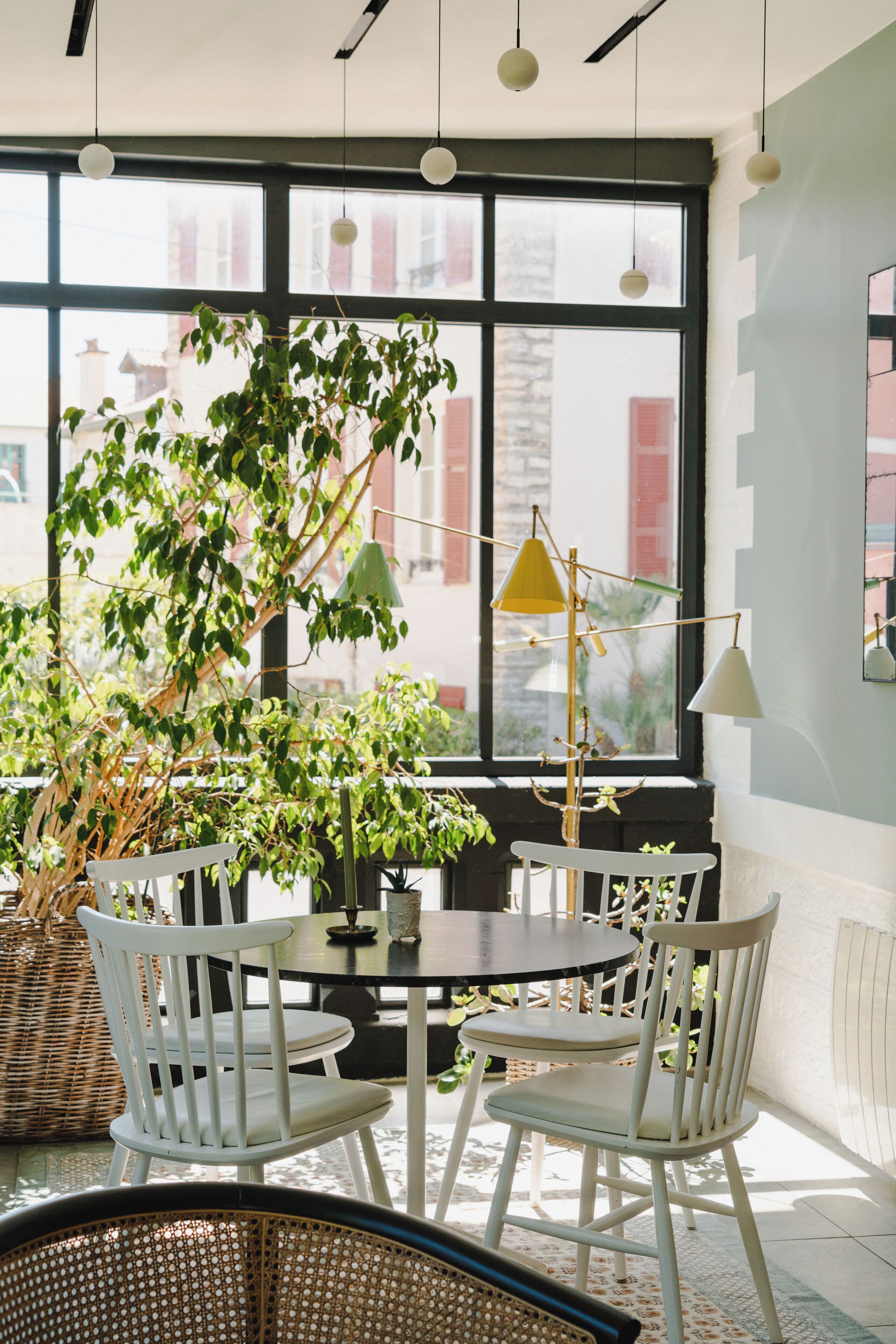 A room with a large window, white chairs, a round table, and hanging pendant lights.