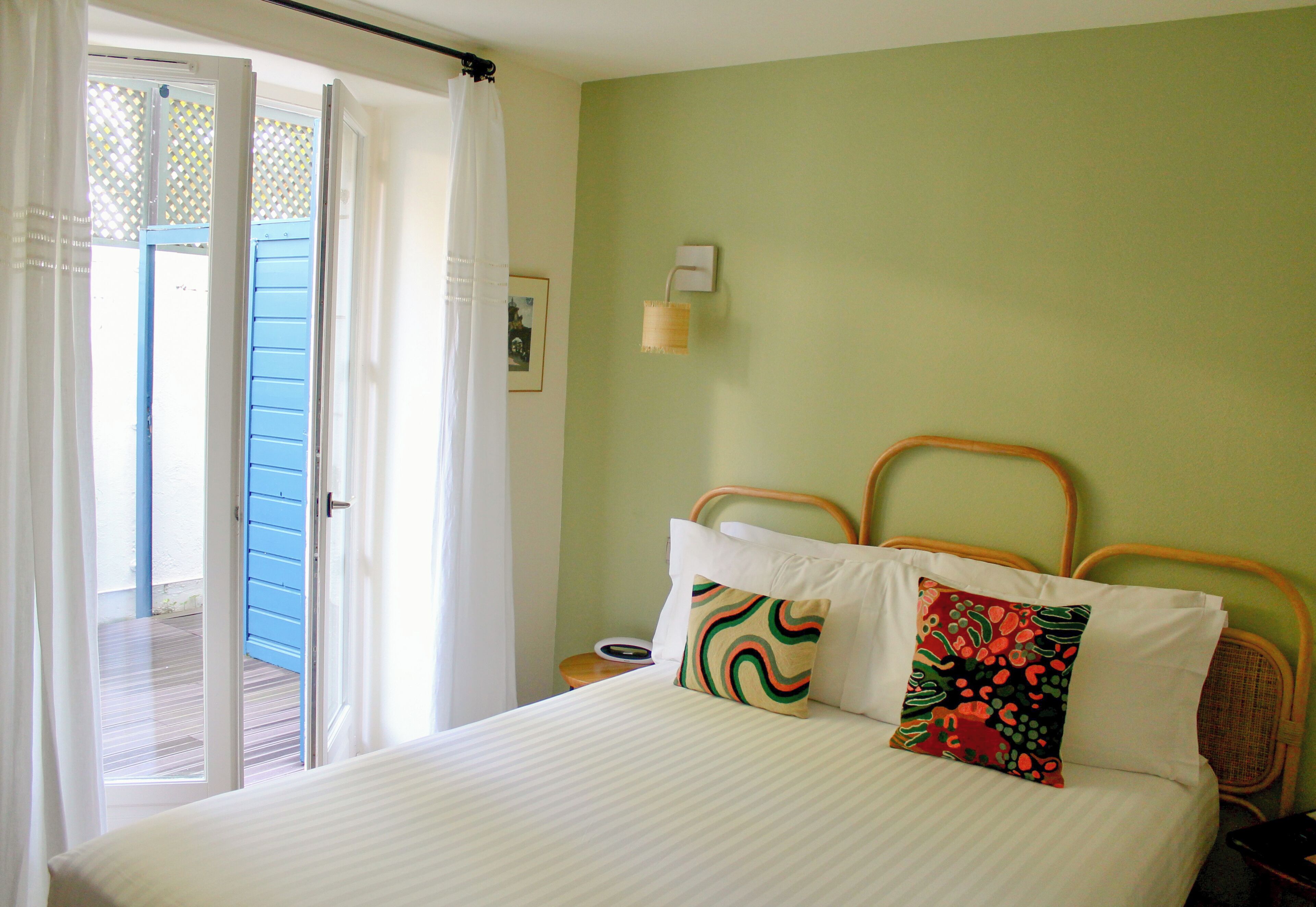 A bedroom with a bed, pillows, a nightstand, a lamp, and a view of the outside.