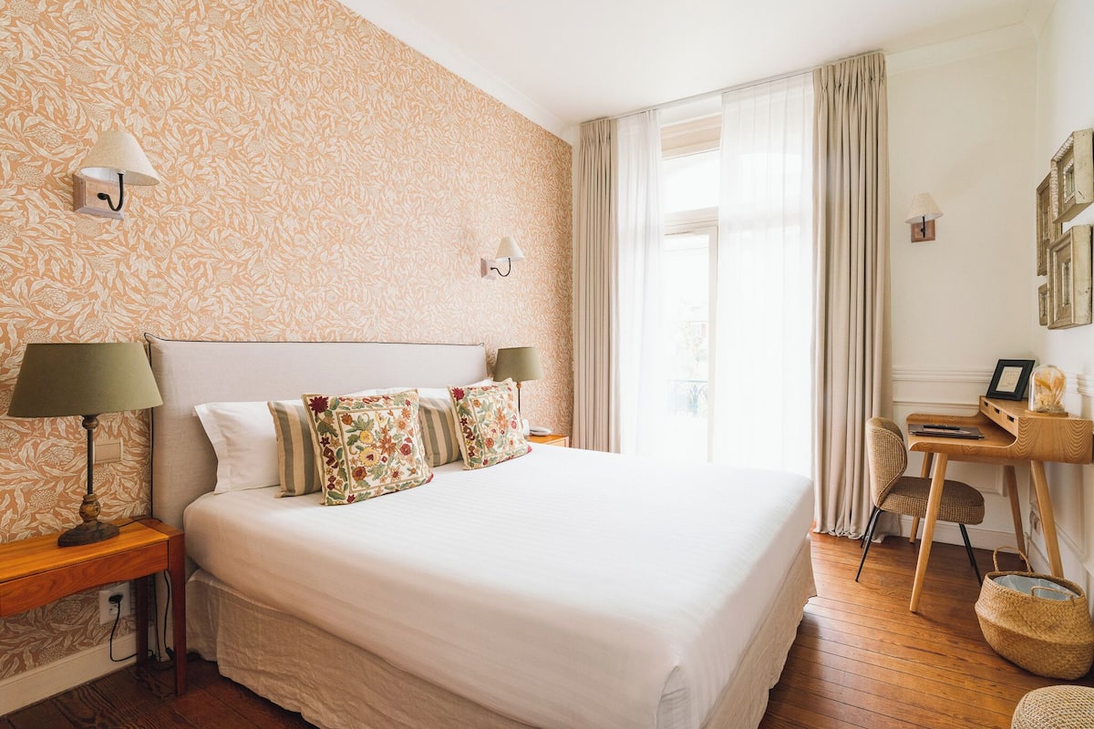 A neatly arranged bedroom with a large bed, a wooden desk, and a chair.