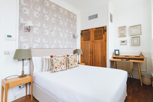 Un dormitorio con una cama, un escritorio de madera, un armario y un papel tapiz estampado.