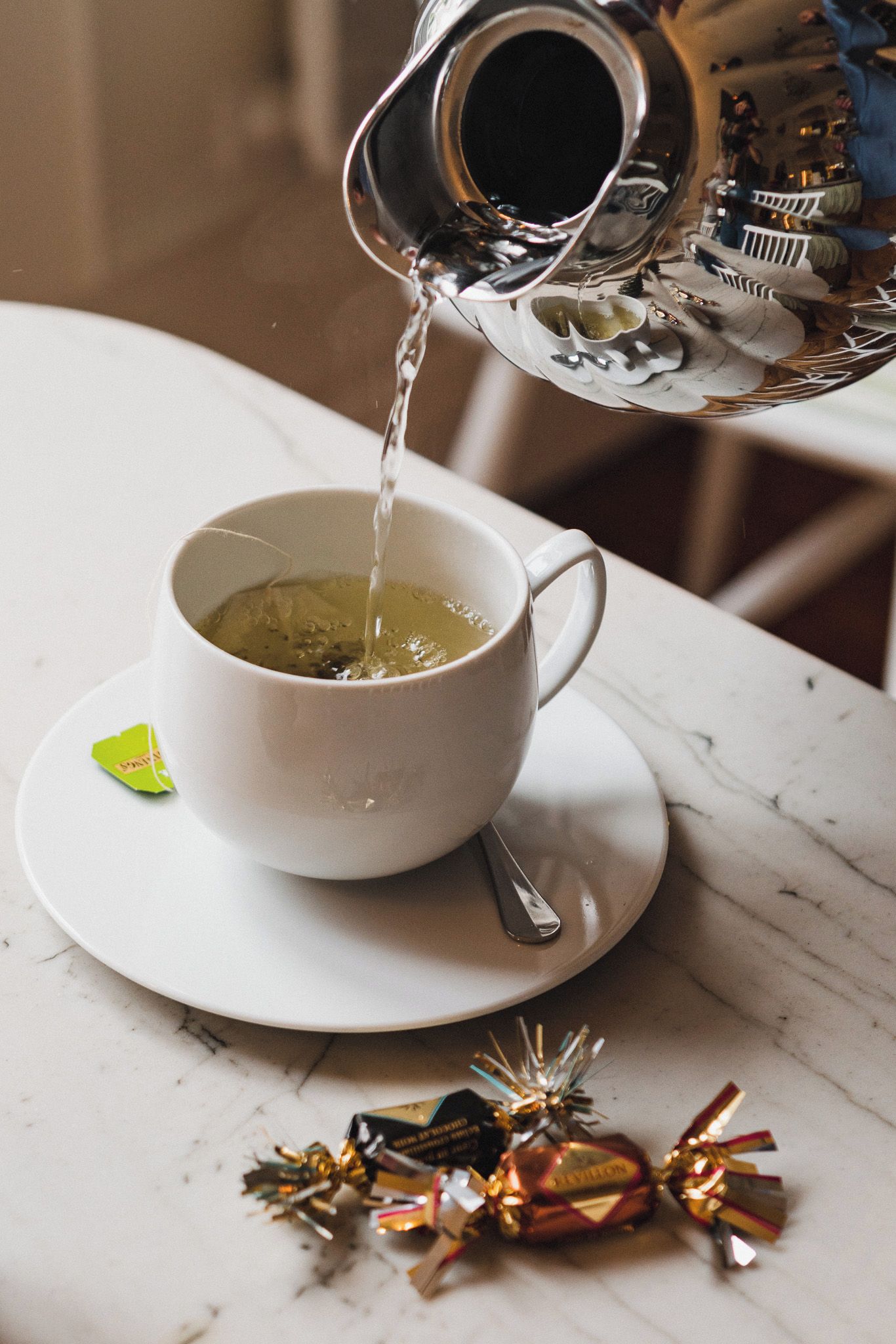 Una taza blanca sobre un plato con una bolsita de té y una cuchara, y un adorno sobre la mesa.
