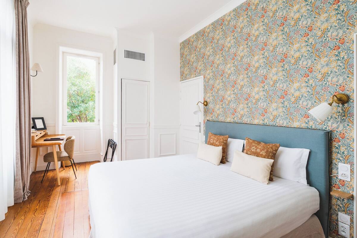 A bedroom with a large bed, a desk with a chair, and a window with curtains.