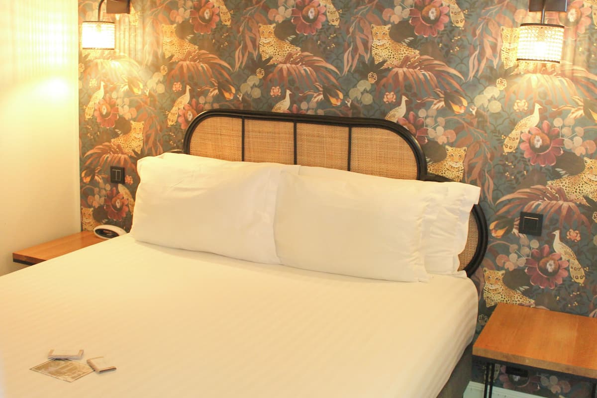 A bed with white linens, a headboard with a woven design, and a floral wallpaper pattern.