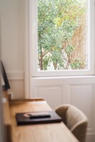 Una habitación con escritorio de madera, una silla y ventana con vistas a un árbol.