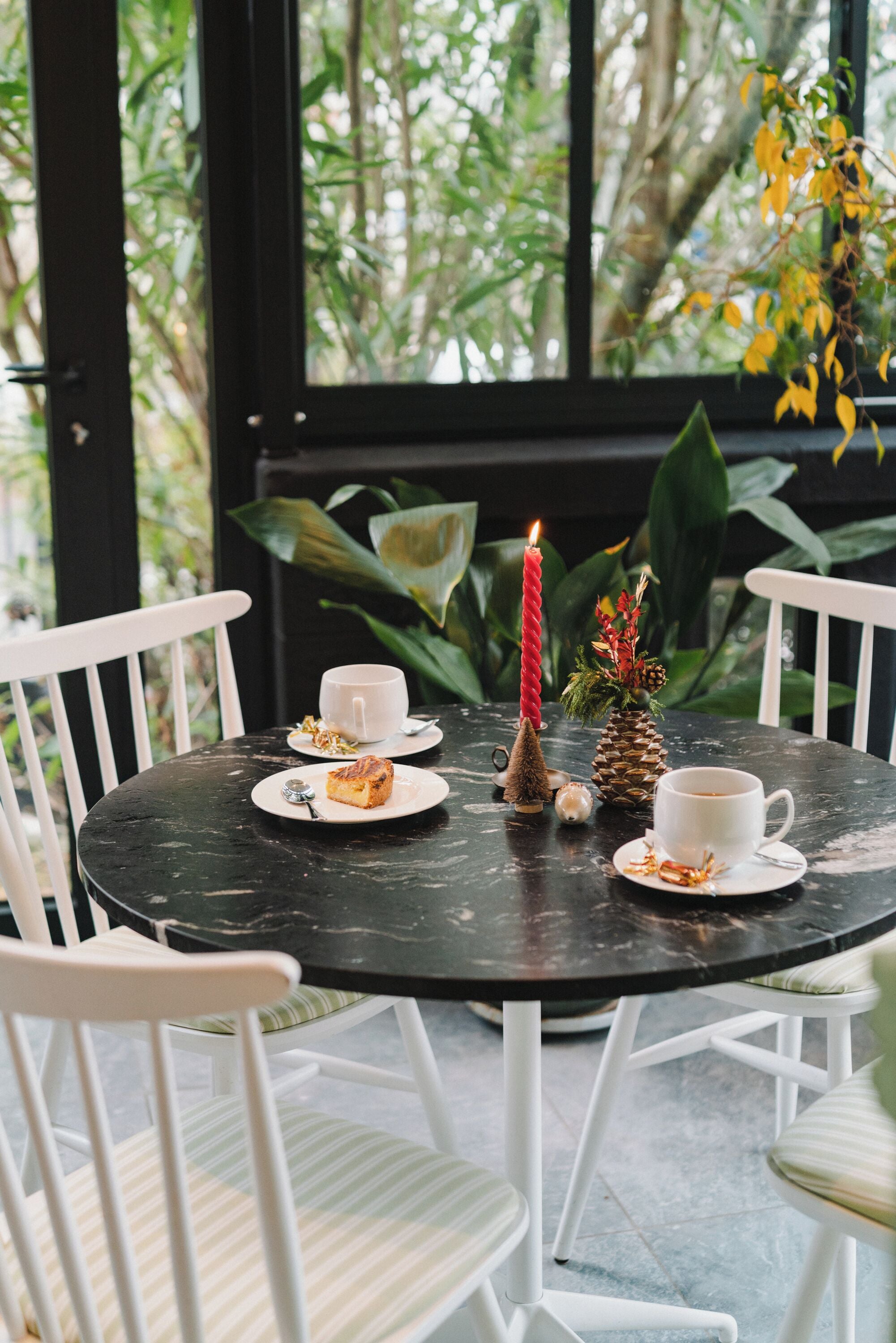 Une table ronde avec des chaises blanches, une bougie et un petit sapin de Noël.