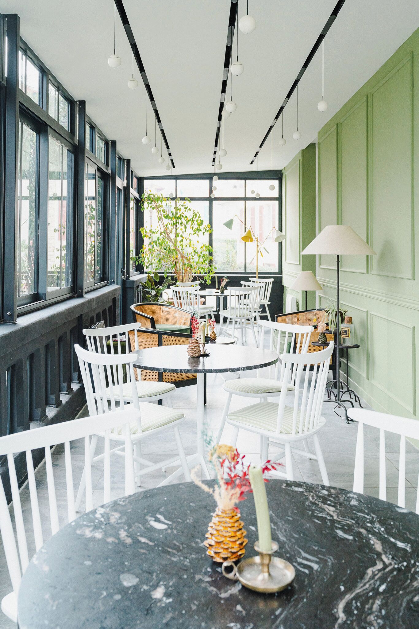 A dining area with round tables and white chairs, large windows, and hanging pendant lights.