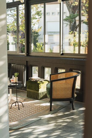 A room with large windows, a wicker chair, a green ottoman, and a small table with a plant. - Hotel Edouard VII (Biarritz)