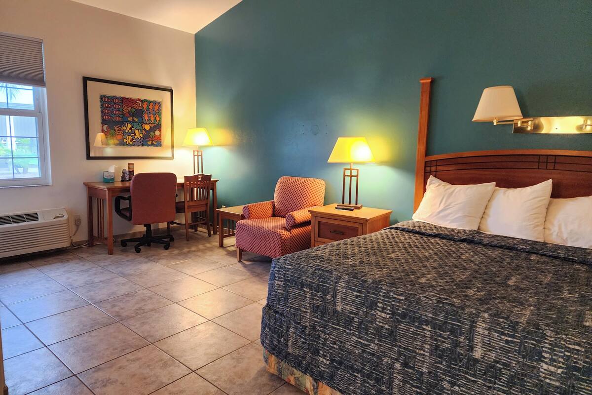 A hotel room with a bed, desk, chair, and two wall-mounted lamps.