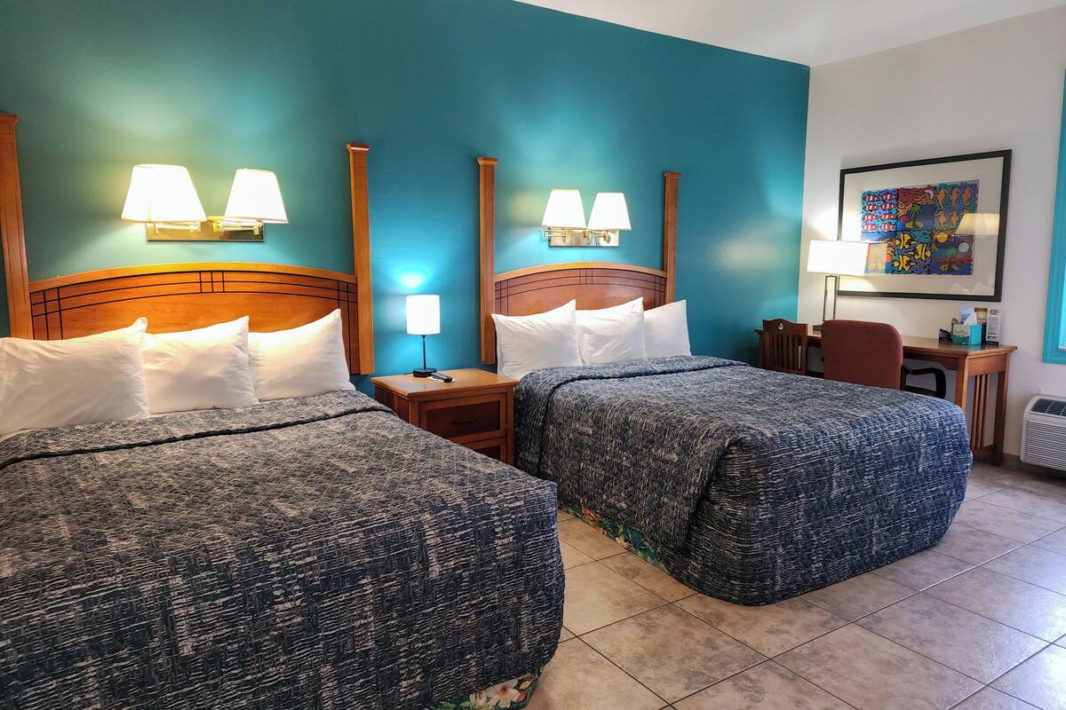 A hotel room with two beds, nightstands, a desk, and a chair.