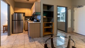 A modern kitchen with a built-in refrigerator, microwave, and coffee maker. There is a glass dining table with chairs.